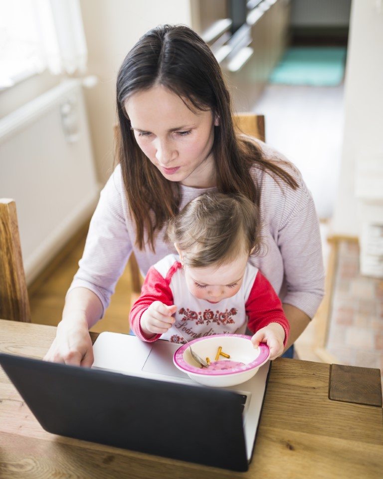 elevated-view-cute-baby-girl-eating-food-while-her-mother-using-laptop
