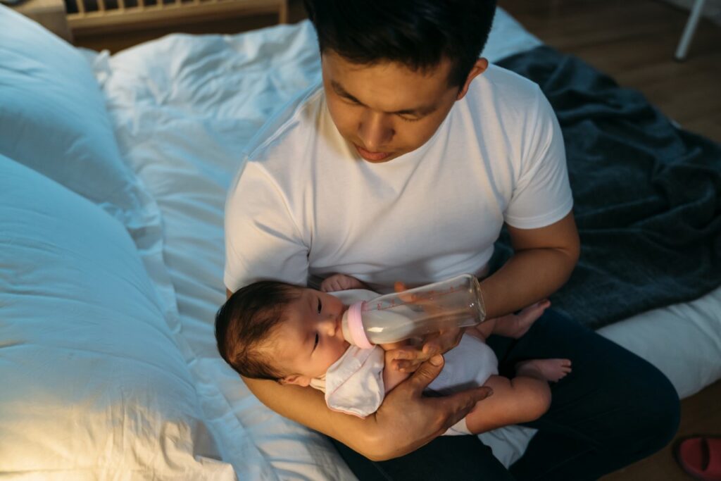 high-angle-shot-loving-taiwanese-father-is-holding-giving-his-newborn-daughter-bottled-milk-bedside-during-bedtime-dark-bedroom-home