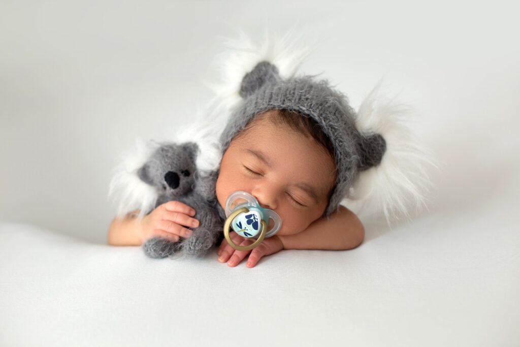 newborn-babyboy-cute-little-resting-baby-with-grey-hat-grey-toy-bear-his-hand-pacifier-his-mouth-white-floor